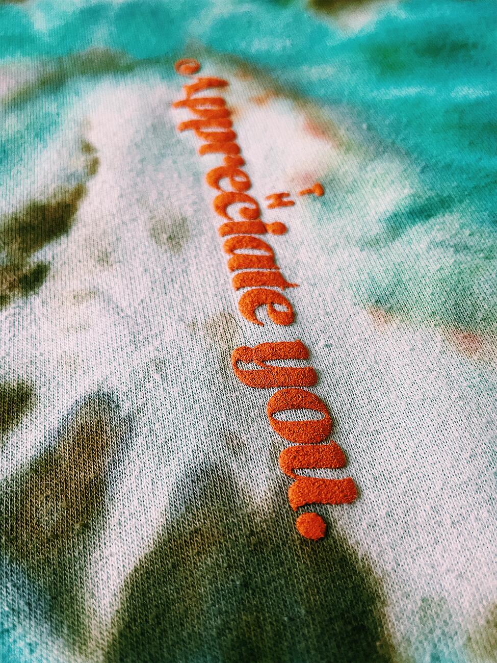 Extreme macro of “Appreciate you.” puff-printed on green and white tie-dye fleece
