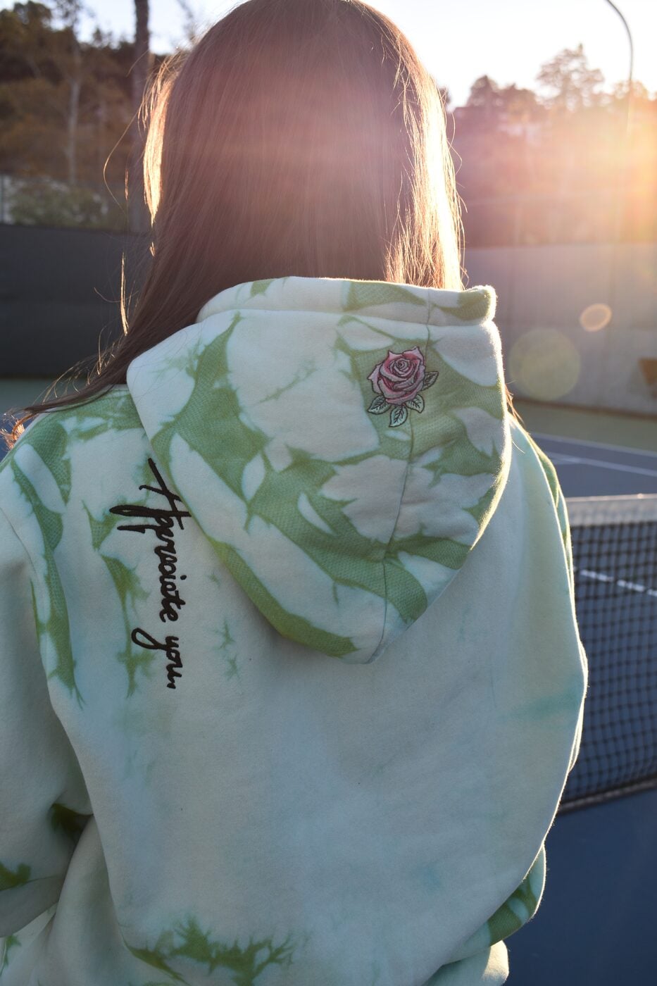 Back of a green tie-dye hoodie with “Appreciate you.” chain-stitched down the shoulder, backlit at golden hour