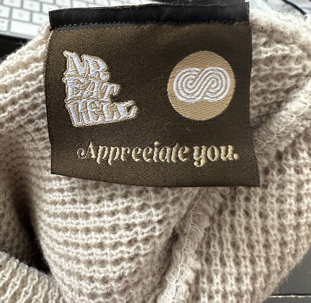 Macro of a woven olive neck tag on cream waffle knit reading “Appreciate you.”