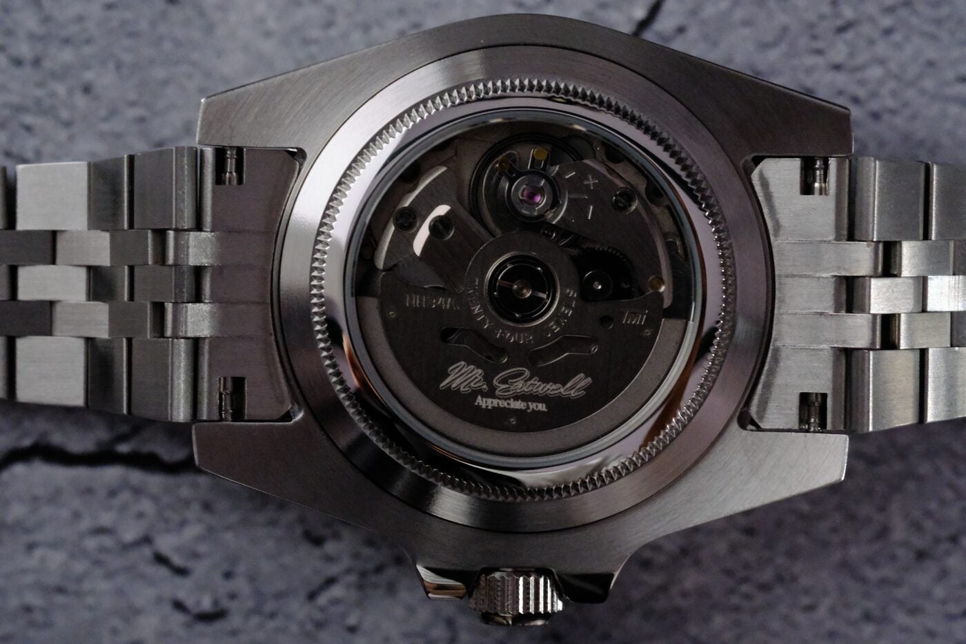 Watch caseback on grey concrete, rotor engraved “Mr. Eatwell / Appreciate you.”
