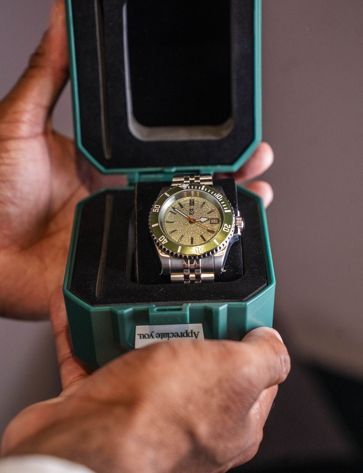 Hands opening a green Mr. Eatwell presentation case with an olive-dial diver inside.