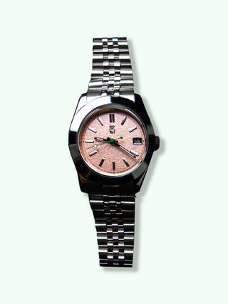Watch with a silver metal band and pink face on a pale green background